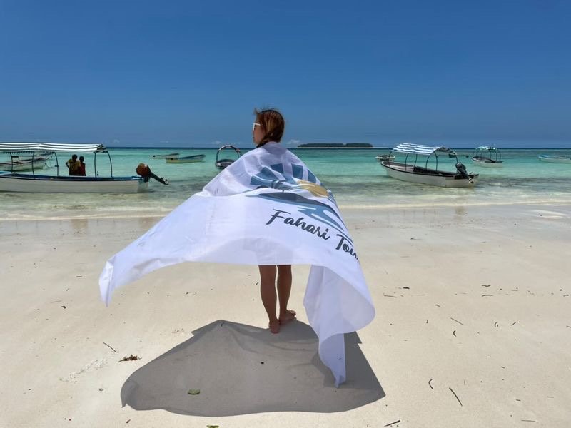 Guest wrapped in the Fahari flag on the beach with boats anchored behind